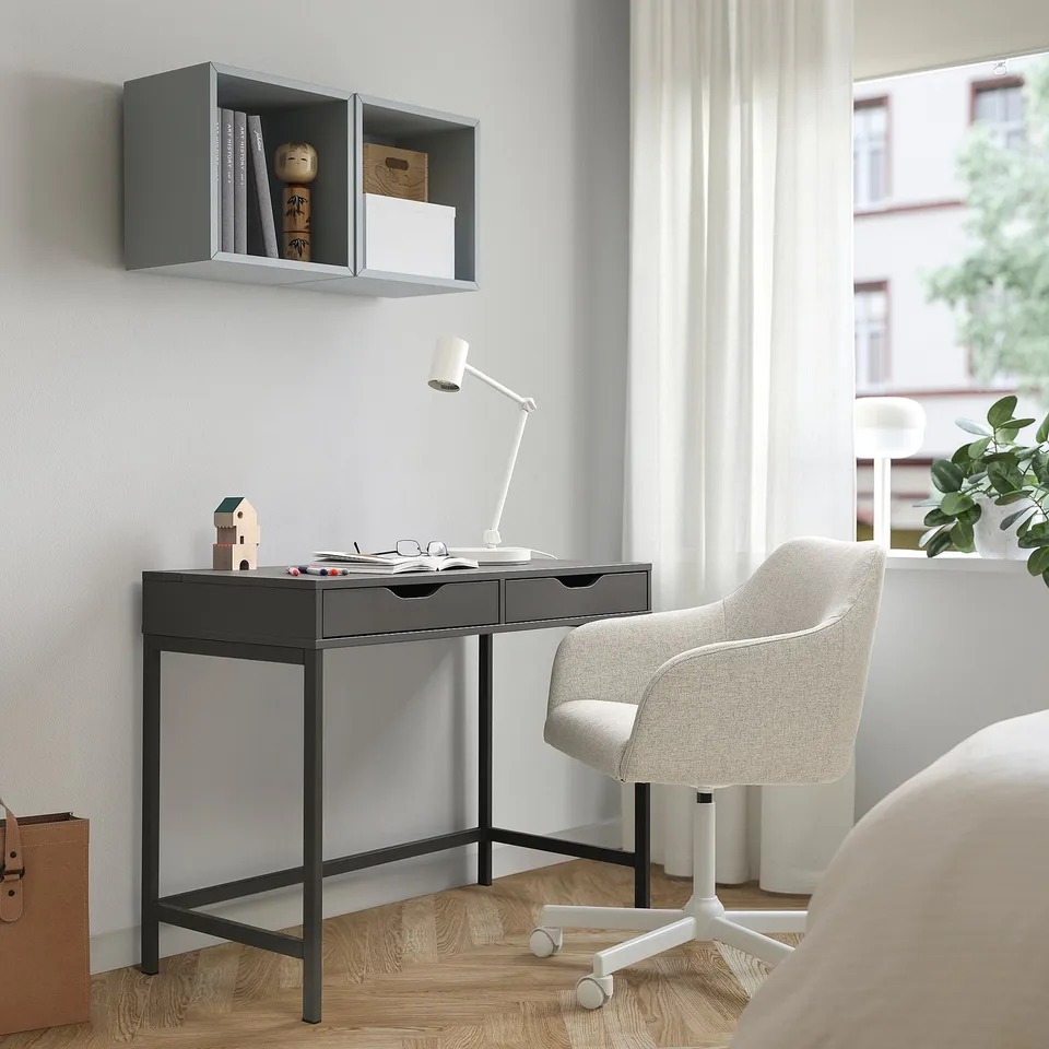 Black ALEX desk with drawers and minimalist design, grey chair, lamp, and shelf, compact for small spaces, window with curtains.