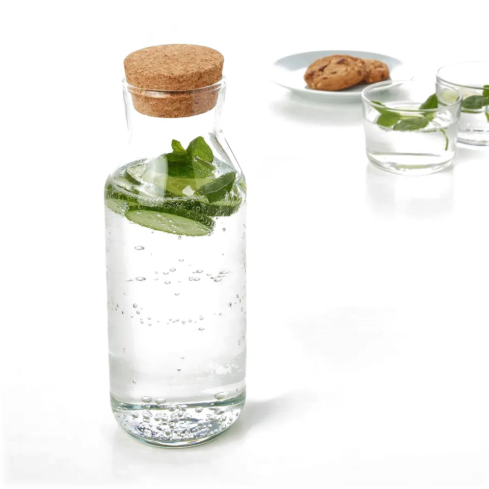 A carafe of water with lemon slices and mint, sealed with a cork lid, sits on a table next to two glasses.