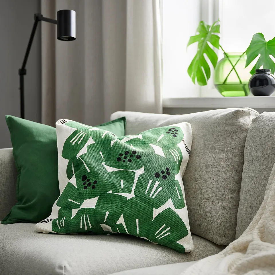 Cosy living room with green leaf pillow on grey sofa, lamp, plant.