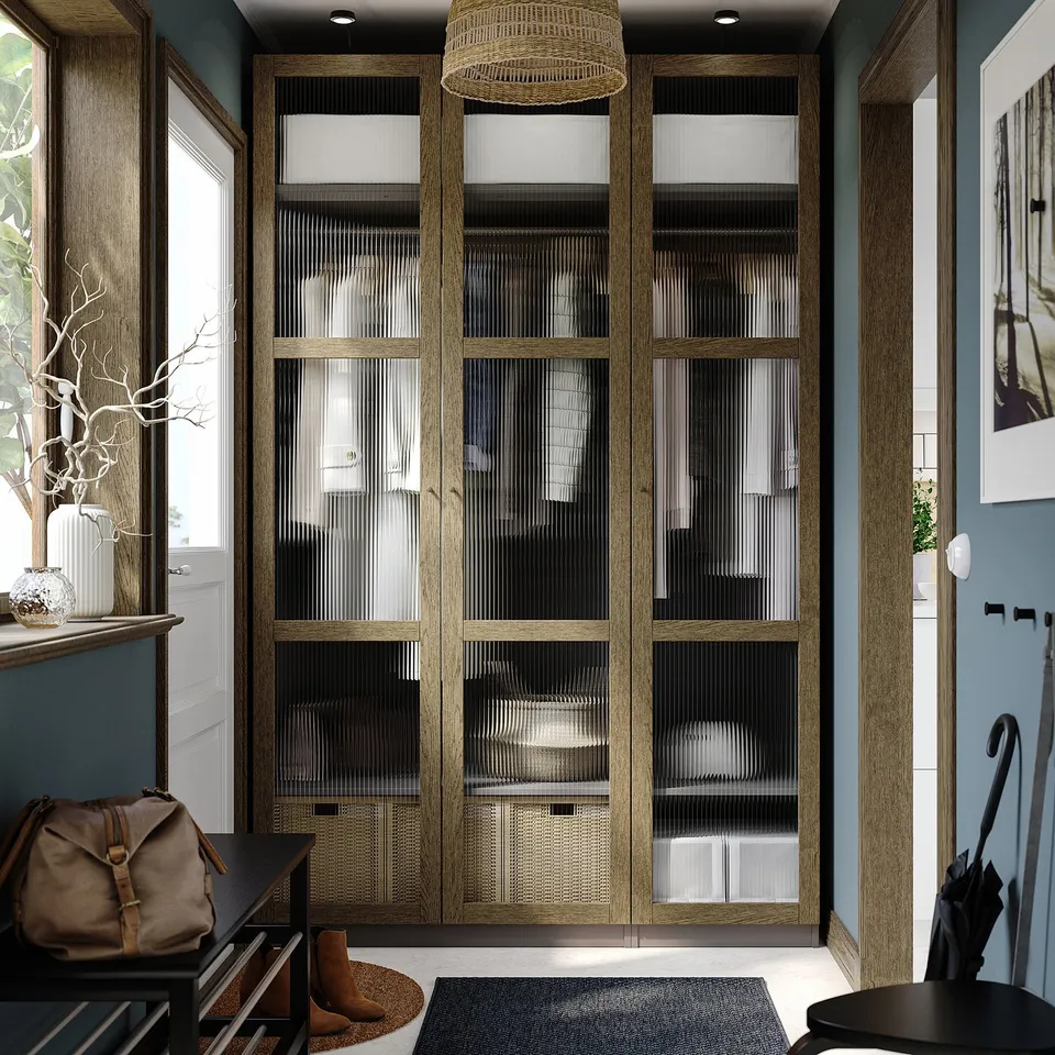 Wooden PAX wardrobe with glass doors, flanked by smaller structures with hanging bag and umbrella, topped with a lampshade.