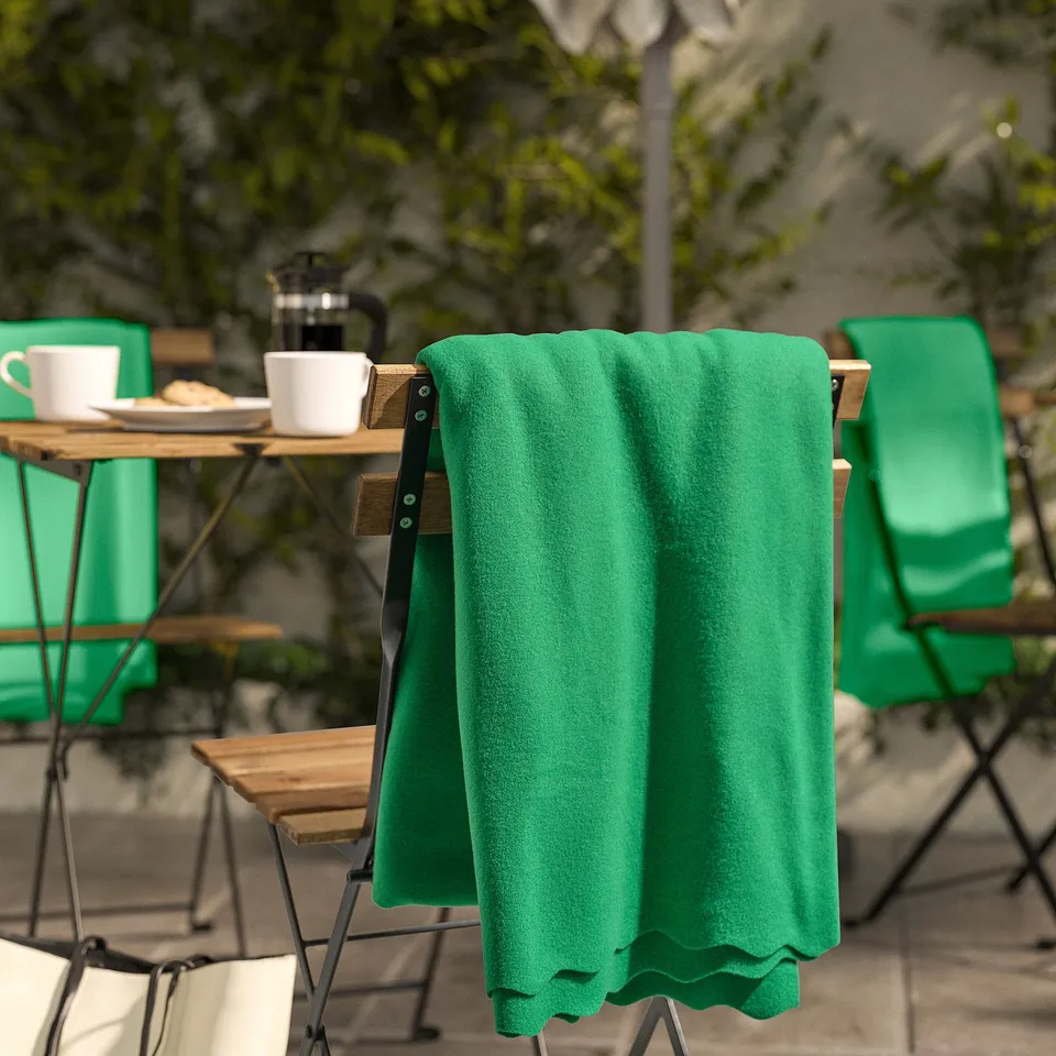 Bright green fleece blanket, soft texture, draped over chair, surrounded by small tables, cups, and plants.