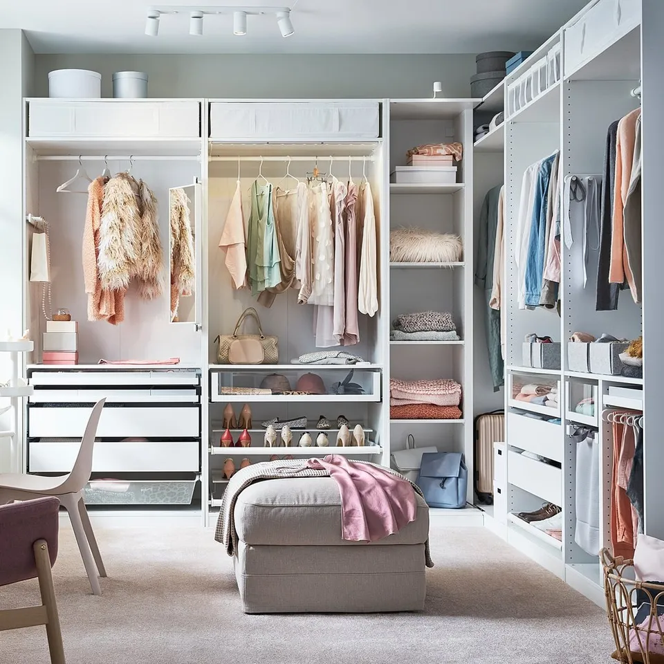 A well-organized bedroom featuring a white PAX wardrobe system with hanging clothes, shelves, and drawers.