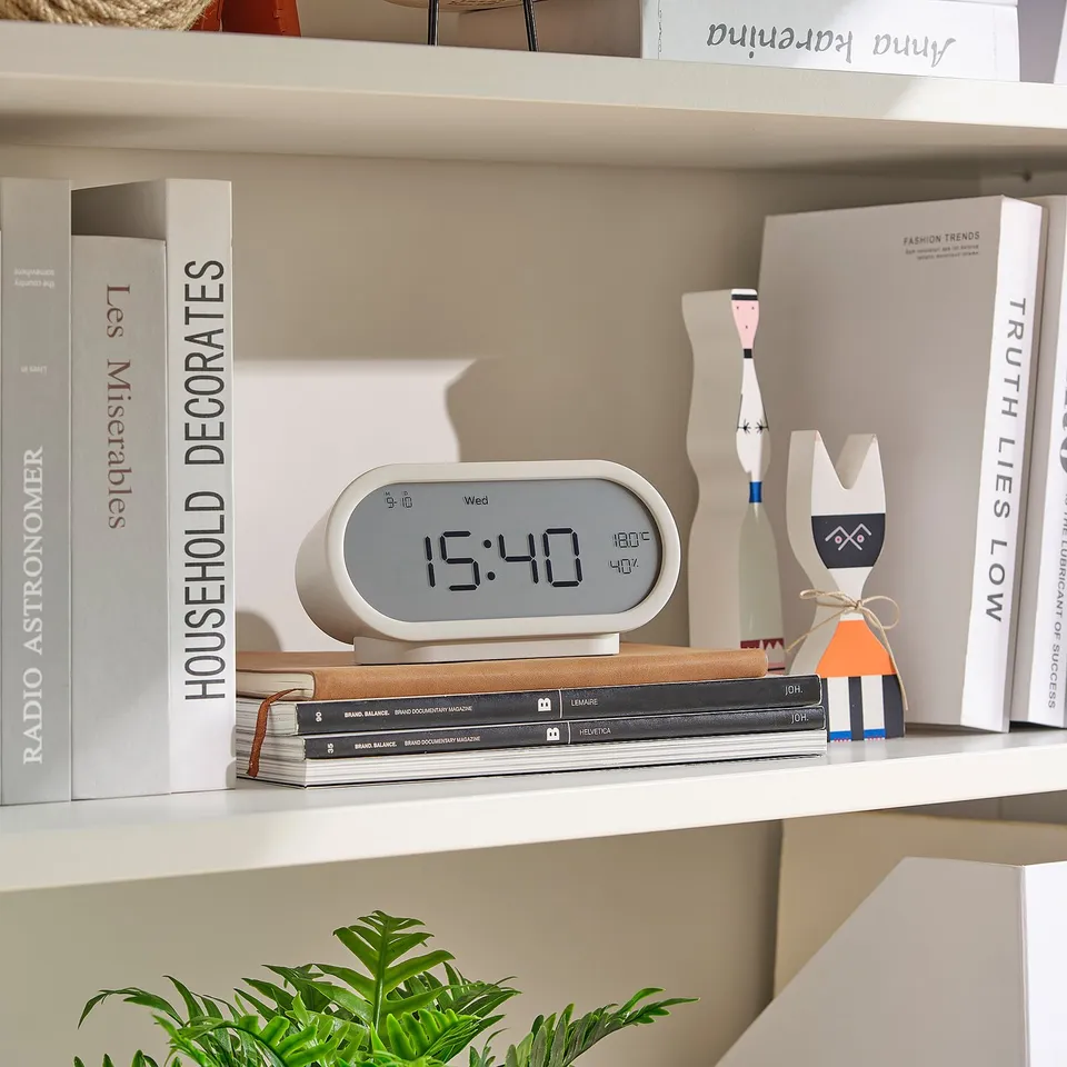 White clock on shelf. Shows time, day, temp, humidity. Modern minimalist design.
