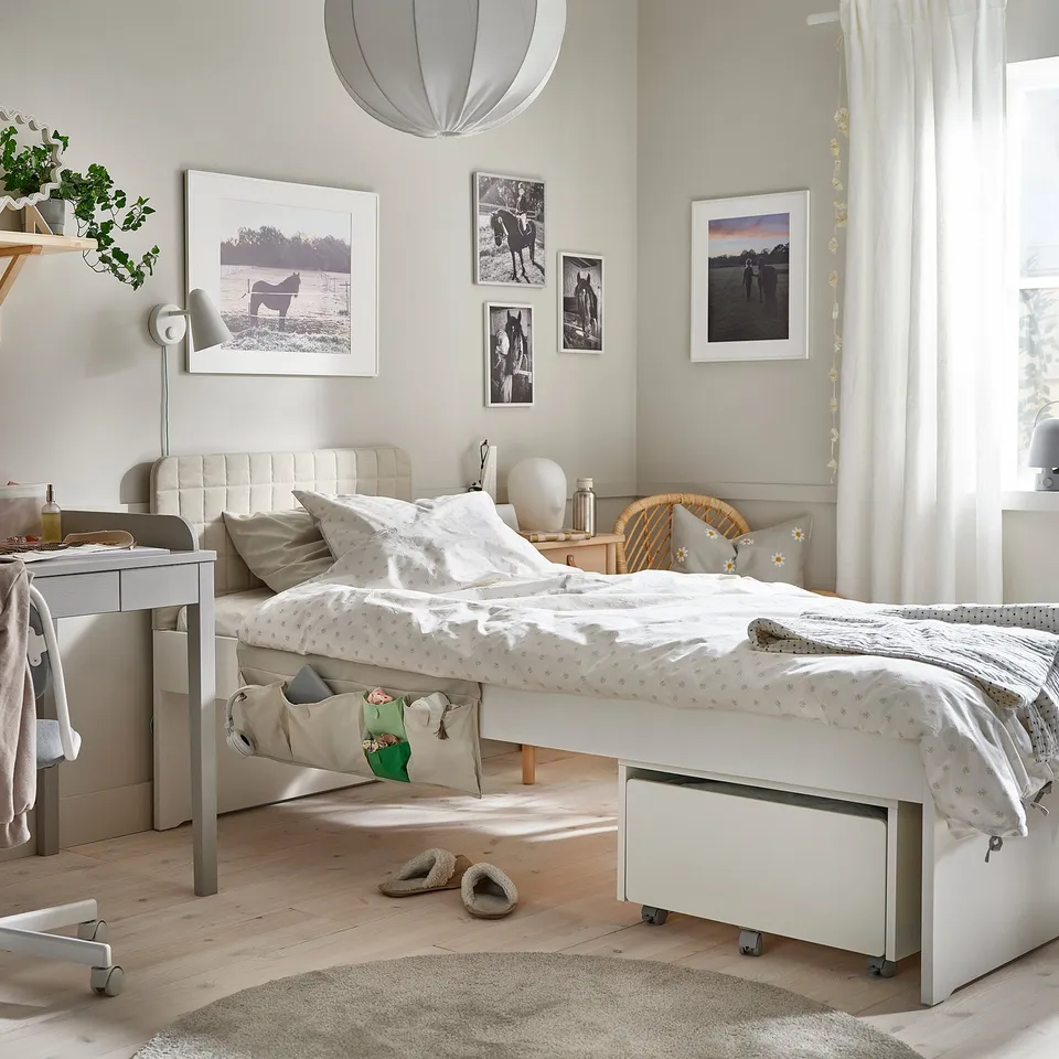 Cosy bedroom with SLÄKT headboard, photos, bed, bedside table, desk lamp, plant, and large window.