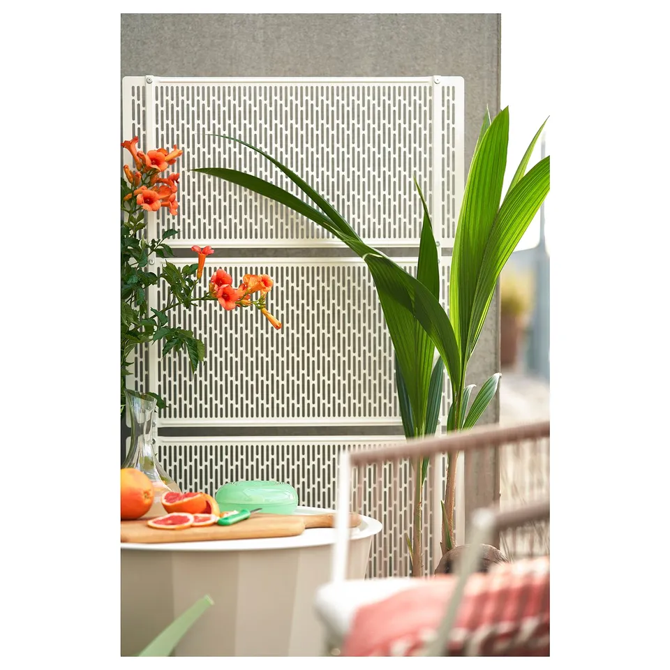 White privacy screen with lattice, steel & plastic, ideal for garden or terrace, with flowers on left, plant on right.