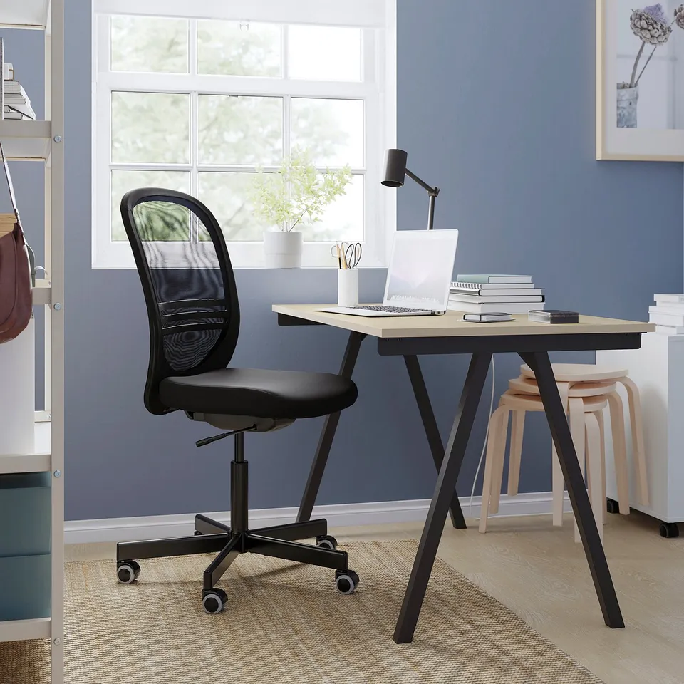 Home office setup: black mesh chair, wooden desk, laptop, books, lamp, plant, blue wall.