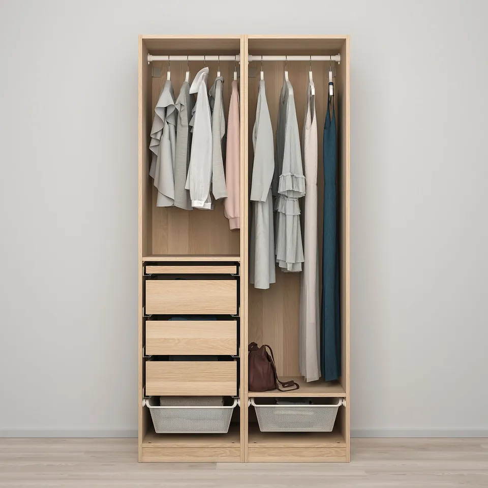 Open wooden wardrobe displaying shirts, dresses, and a handbag. Hanging rail, drawers, and metal baskets.