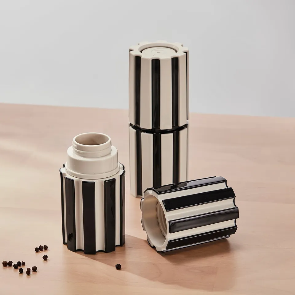 Three striped spice mills on wood. One open, showing contents and scattered peppercorns. Adjustable grind settings.
