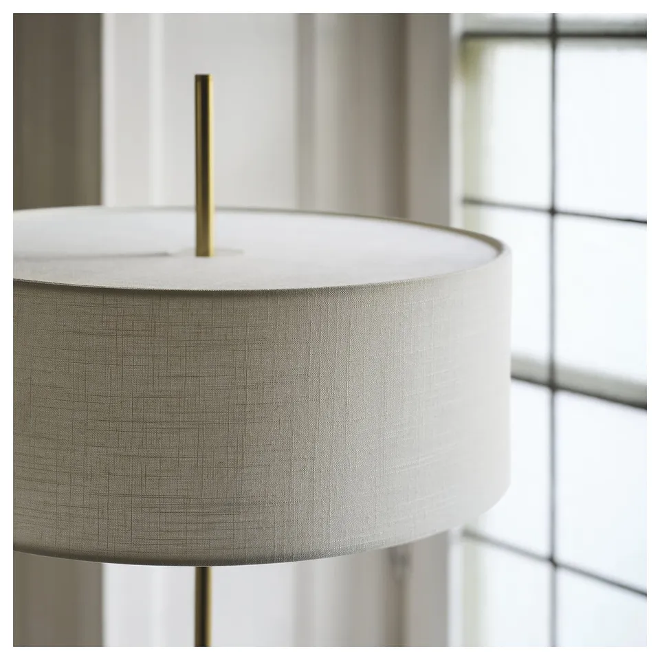 Modern lamp with brass-colored base and fabric shade sits elegantly on a table, providing a sleek and stylish look.