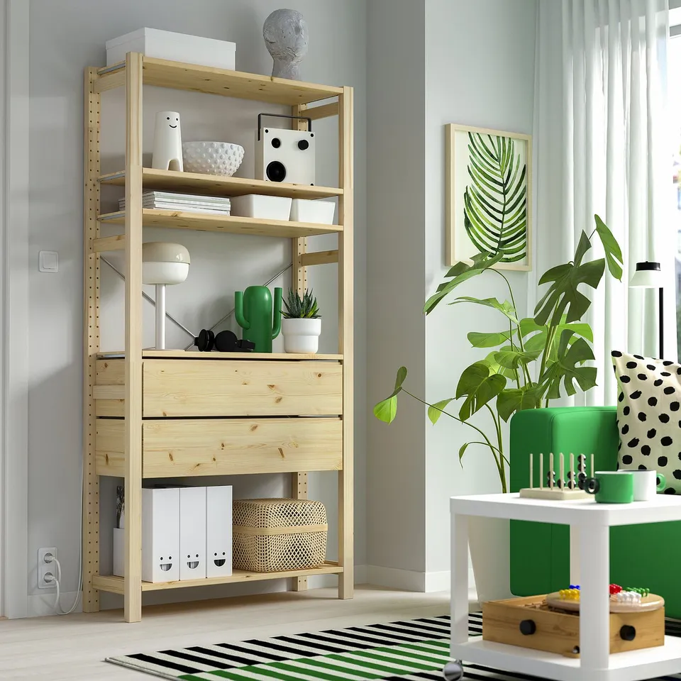 Wooden bookshelf with books, pots, decor, tall plant, leaf art.