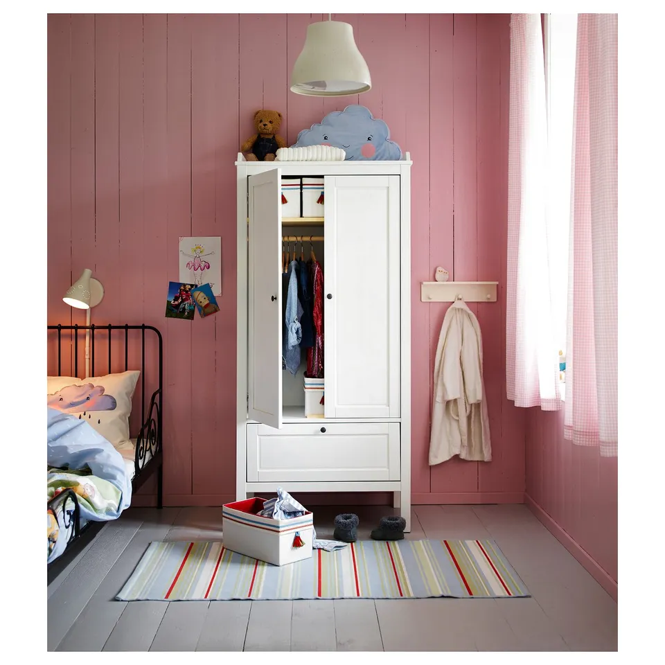 Kids room with white SUNDVIK wardrobe, pink walls, striped rug, small bed, and toys.