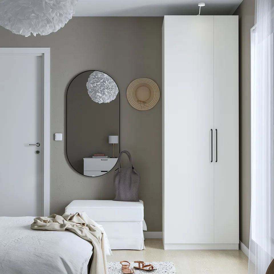A modern bedroom with a sleek PAX white wardrobe, holding space beside a bed.