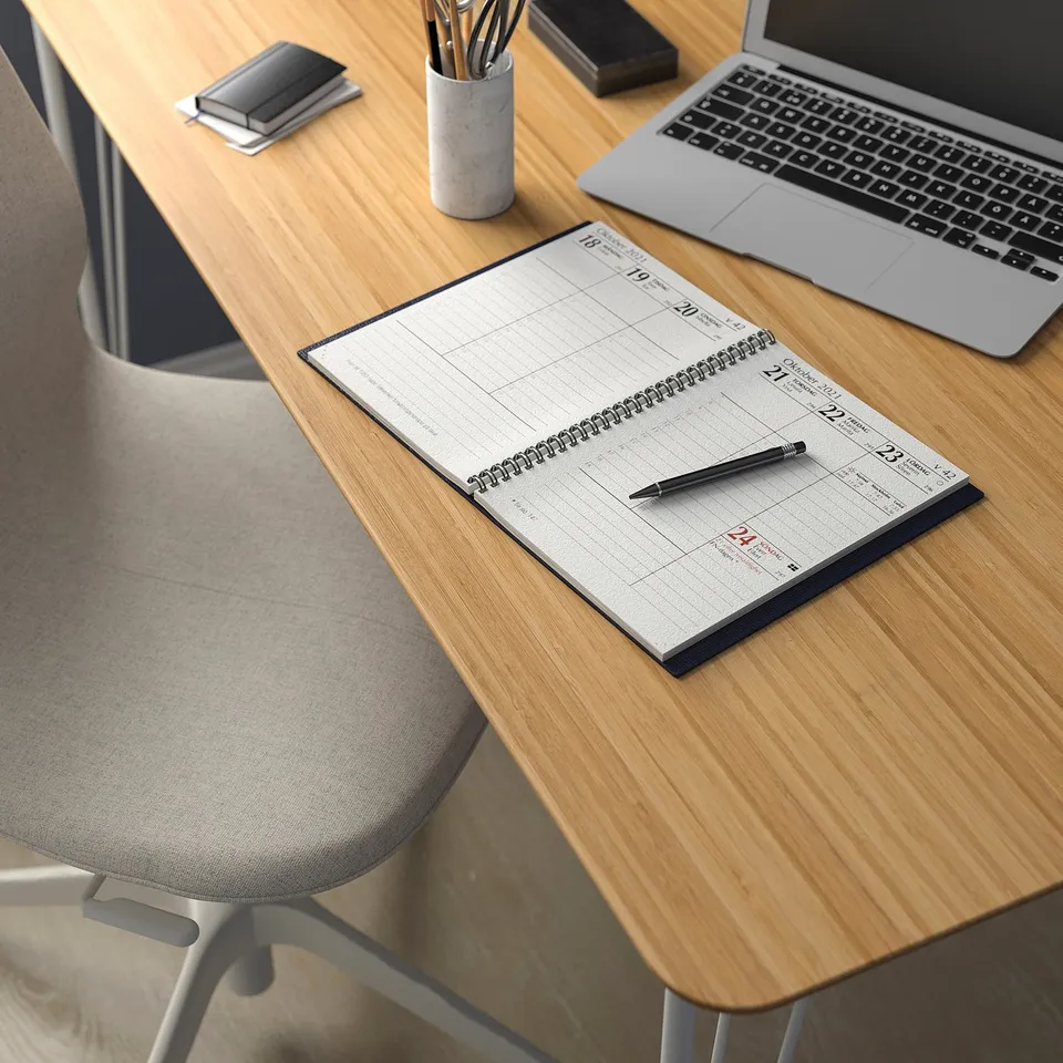 Wooden desk setup with spiral notebook, pen, smartphone, and laptop.