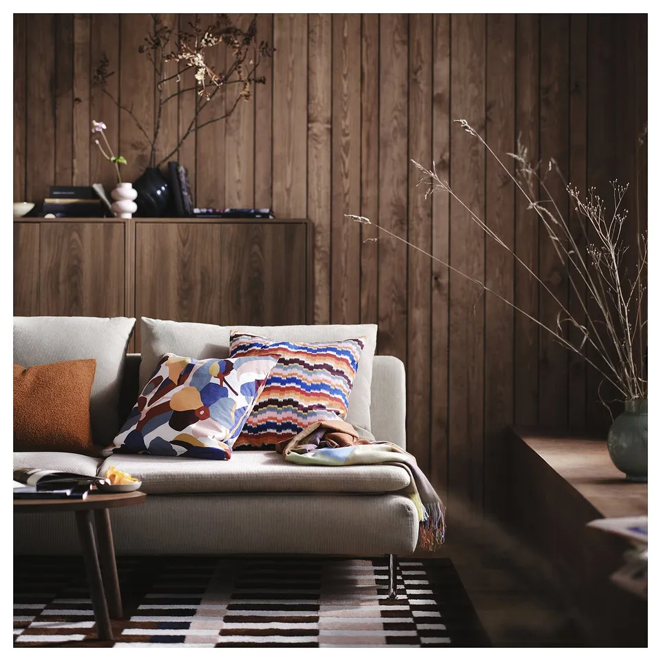 Cosy living room with light grey sofa, colourful patterned pillows, wooden wall panels, and a striped rug.