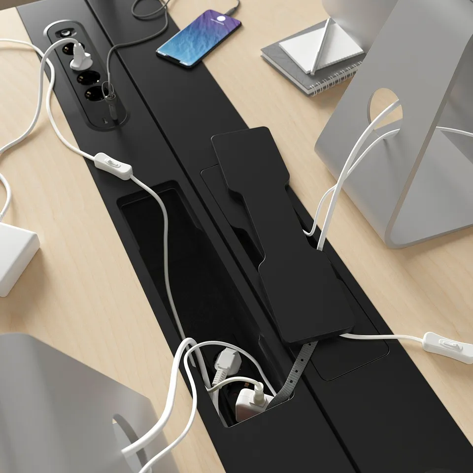 Black MITTZON desk with built-in power sockets and cable management tray. White cords organised, laptop, and phone on top.