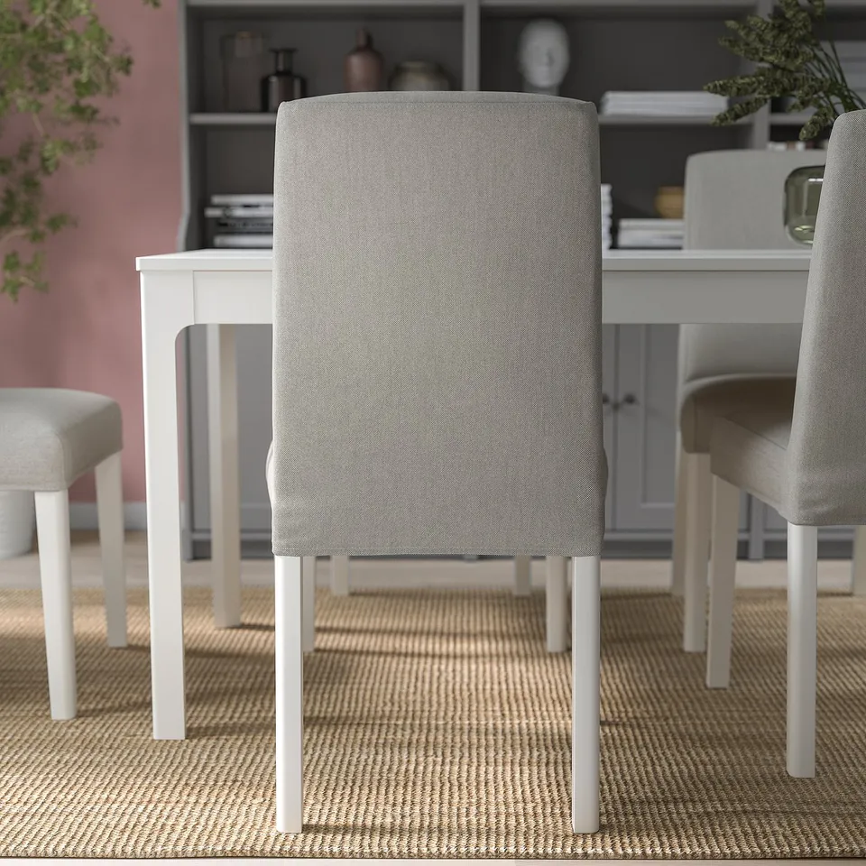 Three light grey upholstered chairs around a white dining table on a woven rug.