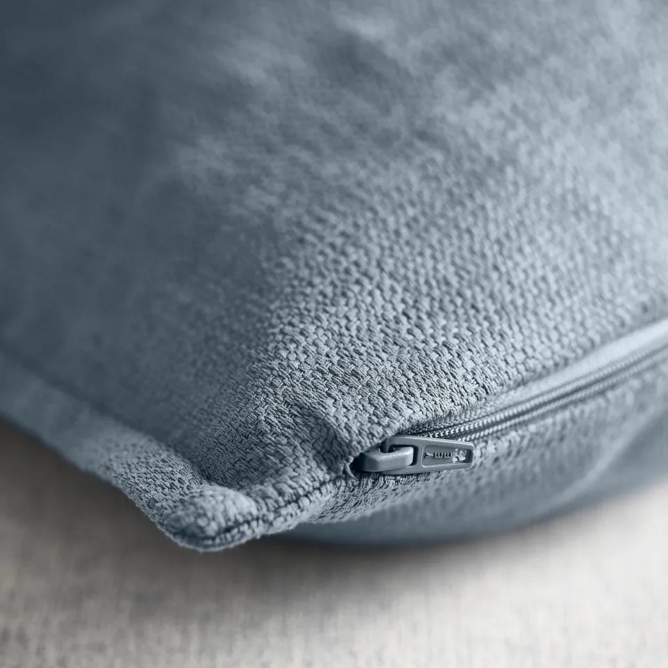 Close-up of luxurious, textured blue-grey cushion cover with zip detail.