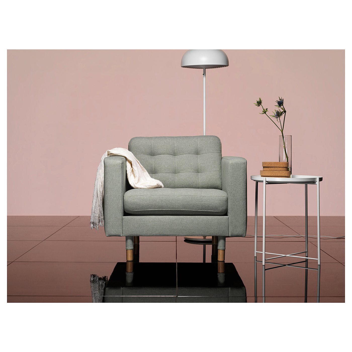 Modern living room a grey, upholstered armchair with wooden legs, positioned near a small table with a flower vase and lamp.
