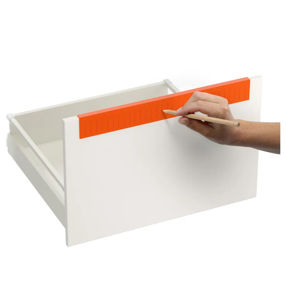 Person using drill template to mark drawer for handles. Template aligns hole positions precisely for mounting knobs and handles.