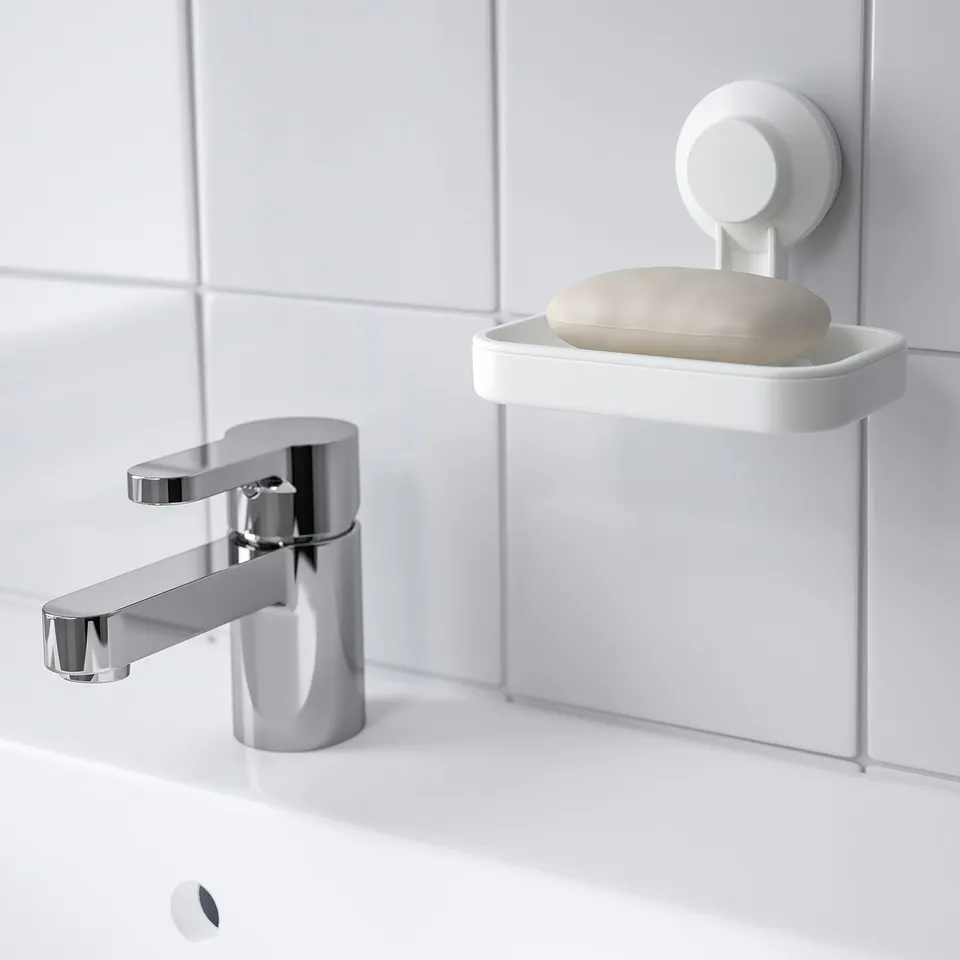 White soap dish with beige soap hangs on tiled wall using suction cup near chrome tap.
