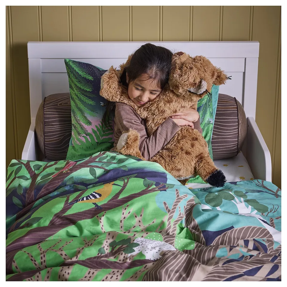 A child hugs a soft lynx toy in bed, showcasing a comforting and huggable cuddly toy with a beautifully patterned quilt.