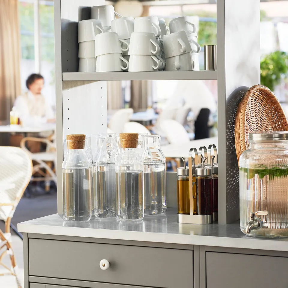 Coffee station with white mugs, clear glass carafes and jugs, and grey shelves. IKEA 365+ glass carafes sit neatly, suitable for fridge.