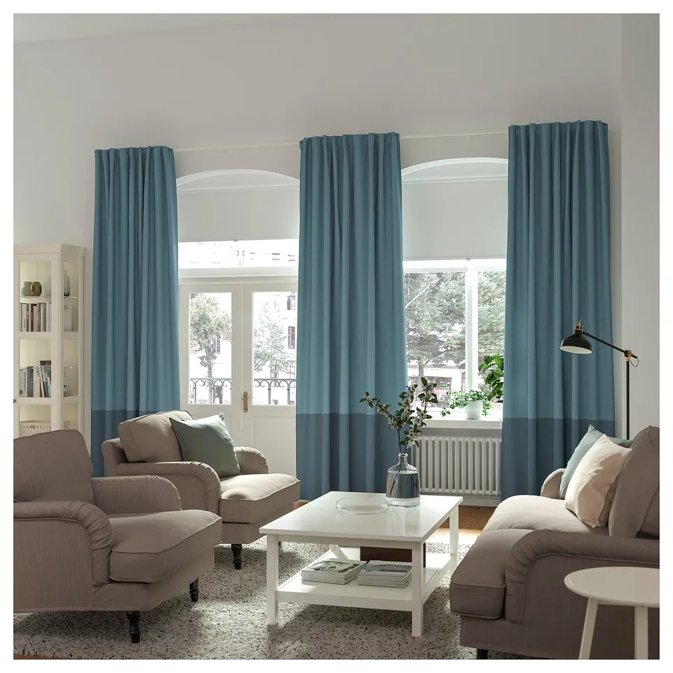 Modern living room with beige sofas, white coffee table, and blue curtains on large windows.