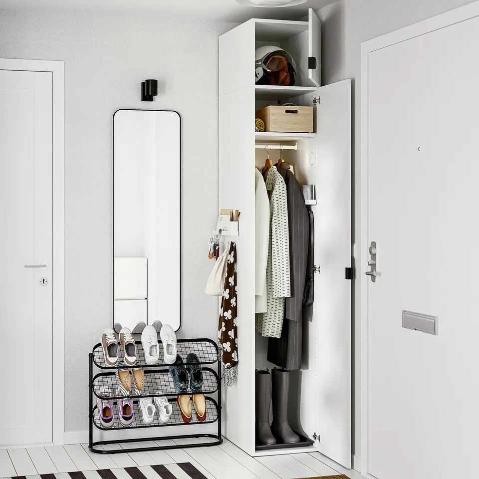 Small, organised entryway with a white closet holding coats and shoes. A tall mirror and shelf unit beside it.