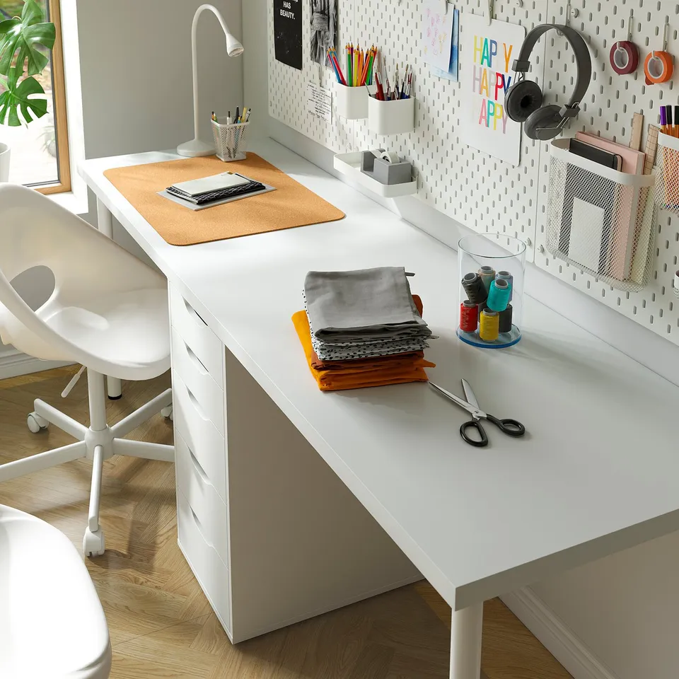 Well-organized desk with a laptop, supplies, and a chair. Includes pegboard with headphones, notes, and crafts.