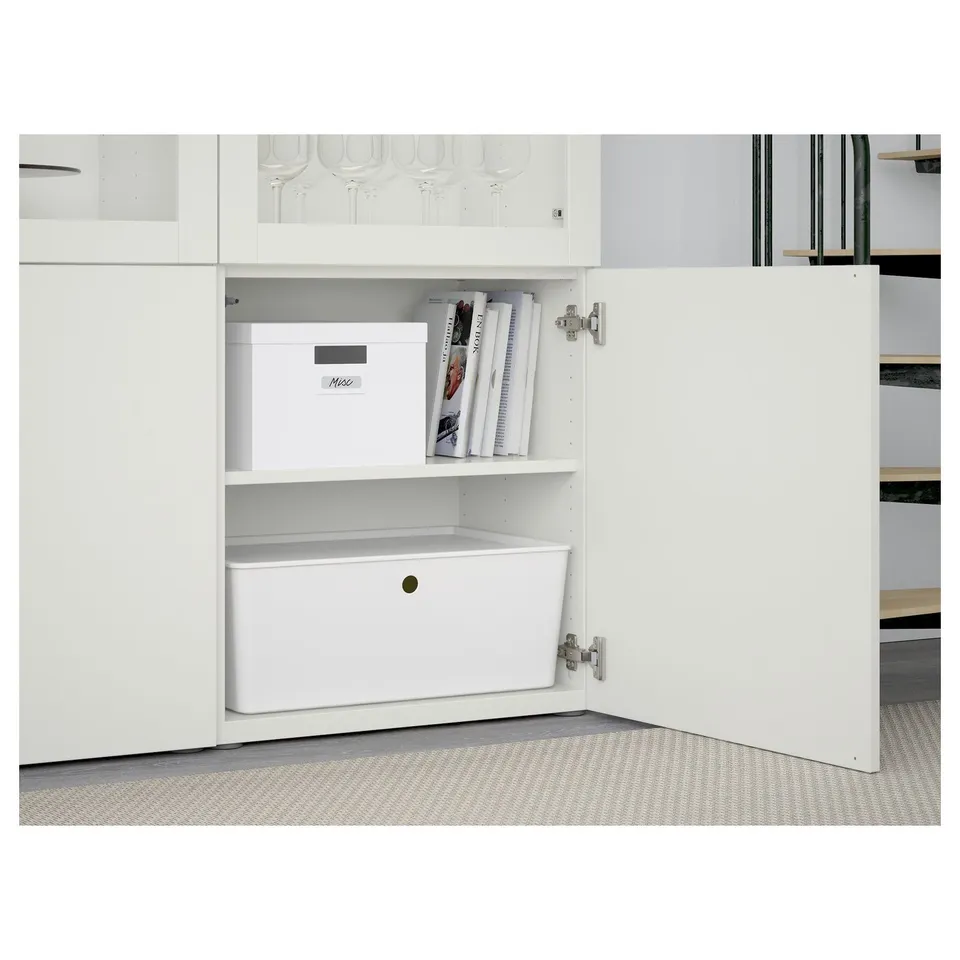 White BESTÅ cabinet with glass doors, open showing storage boxes and magazines inside.