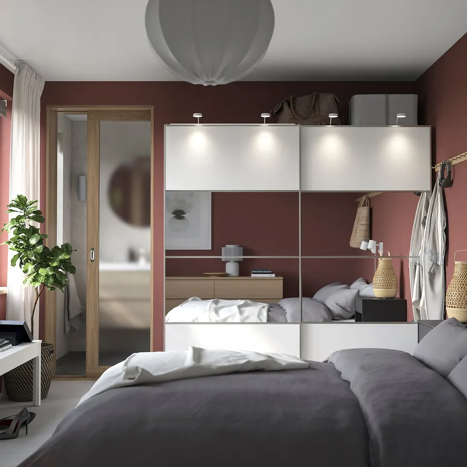 Modern bedroom with red walls, white PAX wardrobe, grey bed, and hanging plants.