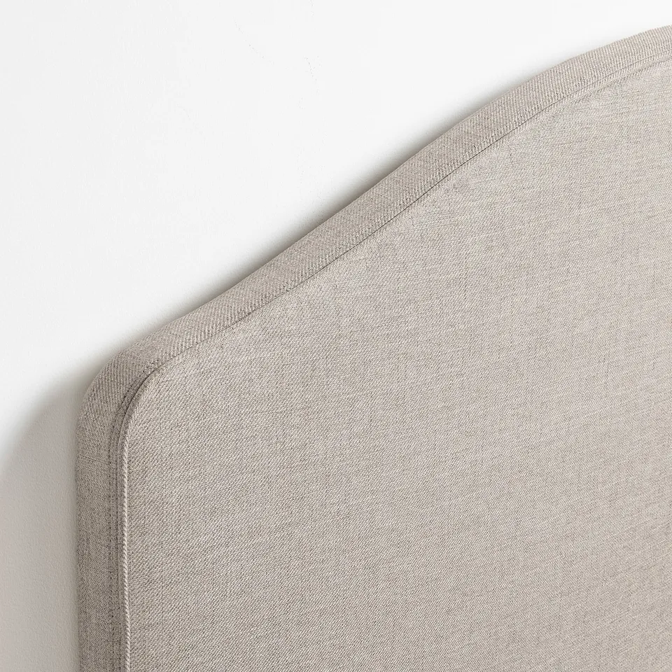 Close-up of a soft, light beige upholstered headboard with neat stitching and smooth fabric, showcasing quality and comfort.