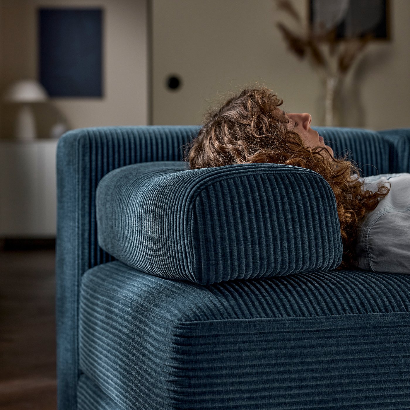 A person lies on a blue JÄTTEBO sofa, using the headrest cushion as a pillow.