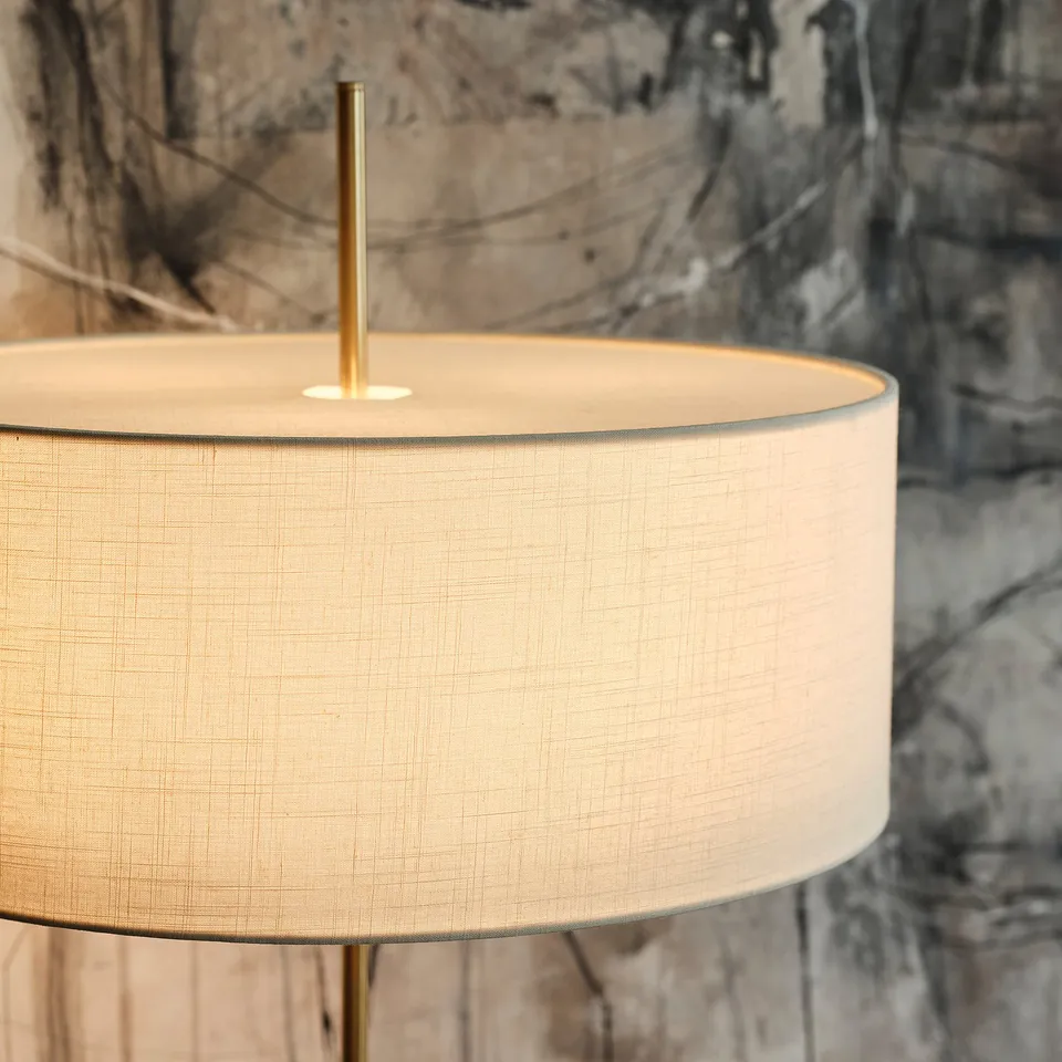 Modern lamp with textured beige shade and brass stand. Elegant, robust design. Natural light tone.