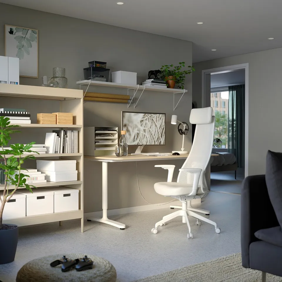 Modern home office setup: white ergonomic chair, wooden desk, bookshelf with plants, grey walls.