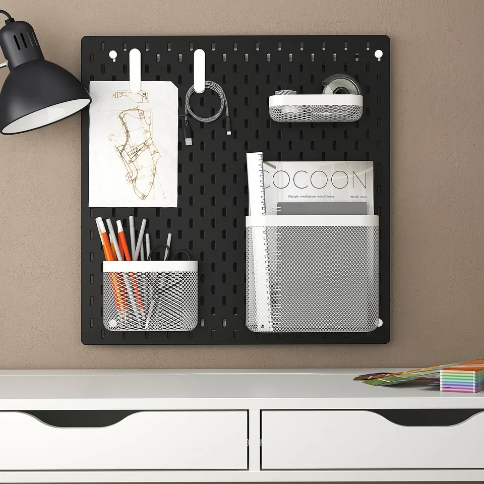 SKÅDIS pegboard with lamp, art, pens, books, speaker. Mounted above a white desk, organised with hooks and baskets.