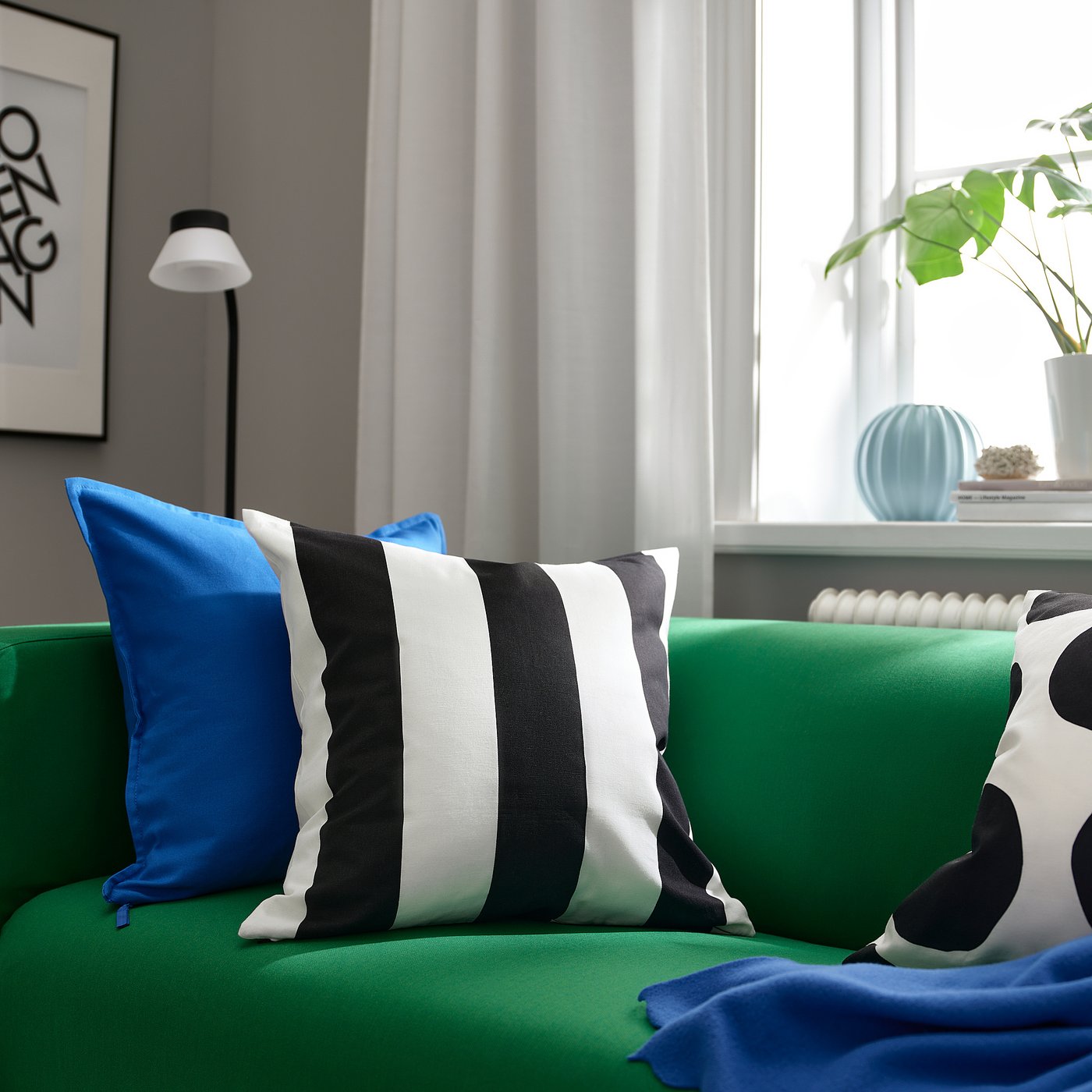 Bright green sofa with black-white striped, blue, and polka dot pillows. Large window with plant and decor.
