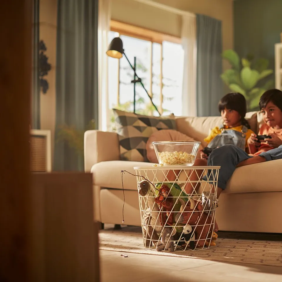 Two boys gaming on VIMLE sofa with snacks. Bright, plant-filled room.
