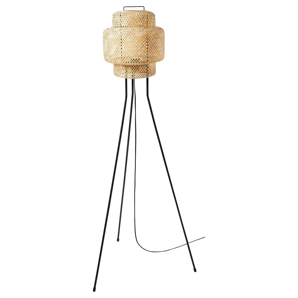 A SINNERLIG floor lamp with a bamboo shade. The lamp has a unique weaved design and stands on three black legs. It is beige in colour.