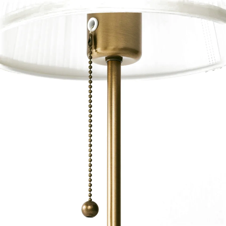 Close-up of ÅRSTID lamps golden metal stem and chain pull.