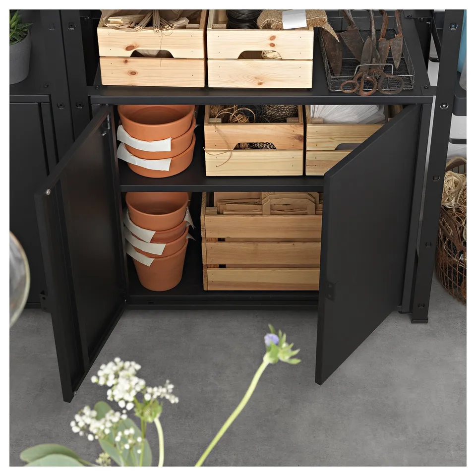 Black storage cabinet with wooden drawers and terracotta pots inside, on a grey floor.
