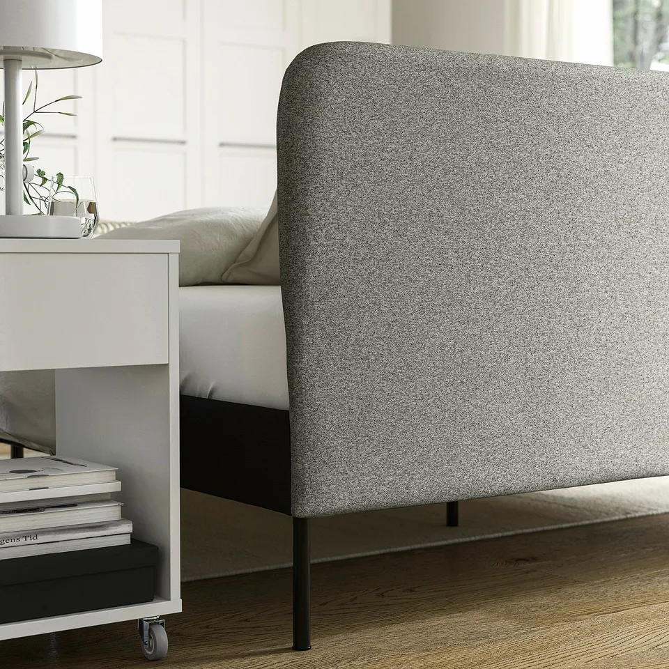 Modern bed frame with grey headboard slipcover, showing functional design with simple ties for easy removal and washing. On wheels for mobility.