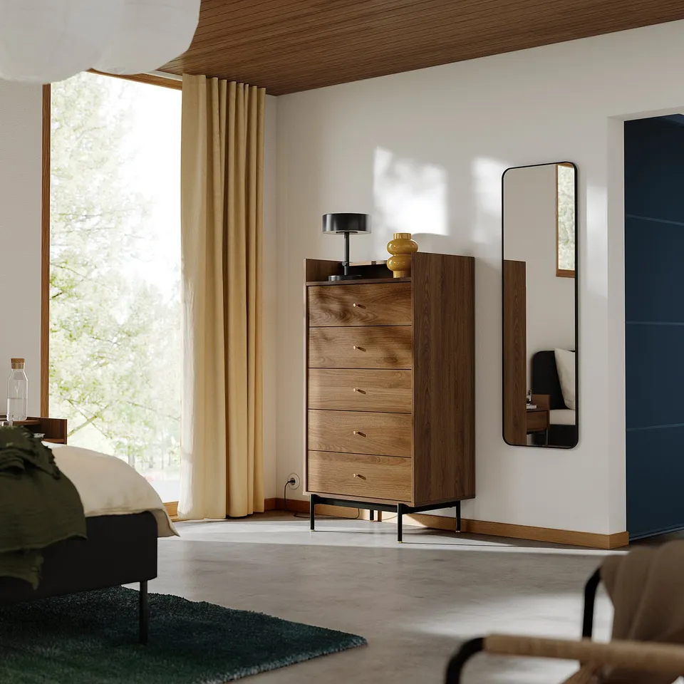 Modern bedroom featuring RÅDMANSÖ dresser with walnut finish, five drawers, and black legs, accompanied by a mirror and a stylish lamp.