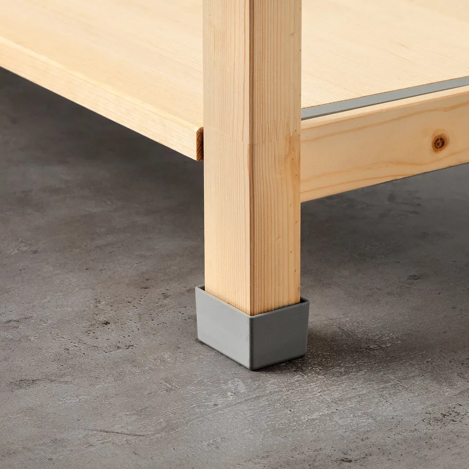 Light wood table leg with silver protective base on rough floor.