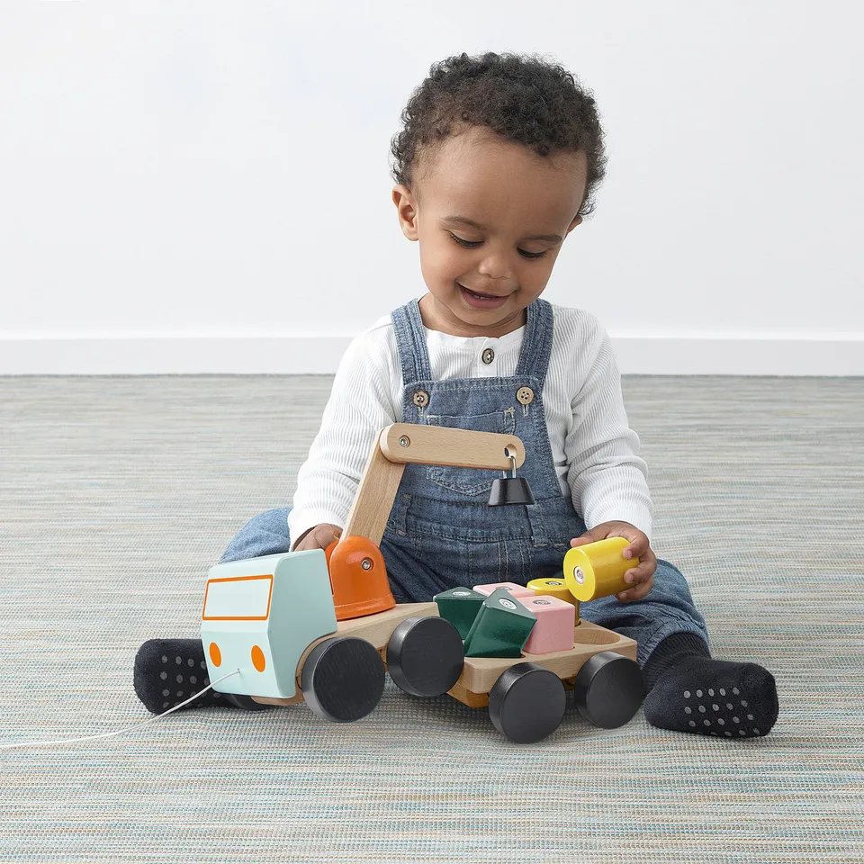 Young child playing with UPPSTÅ wooden toy truck, pulling string, blocks magnetic crane.