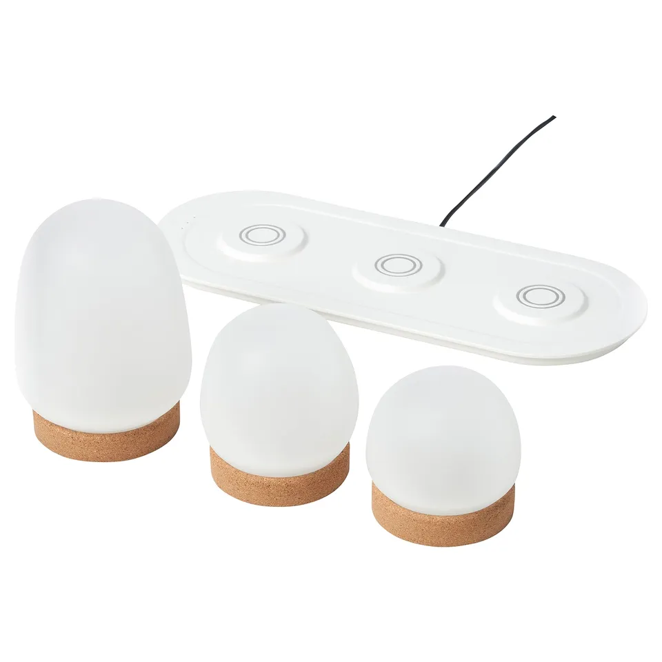 Three white, spherical led lamps on a matching charging tray, with cork bases, offering a modern, minimalist design.