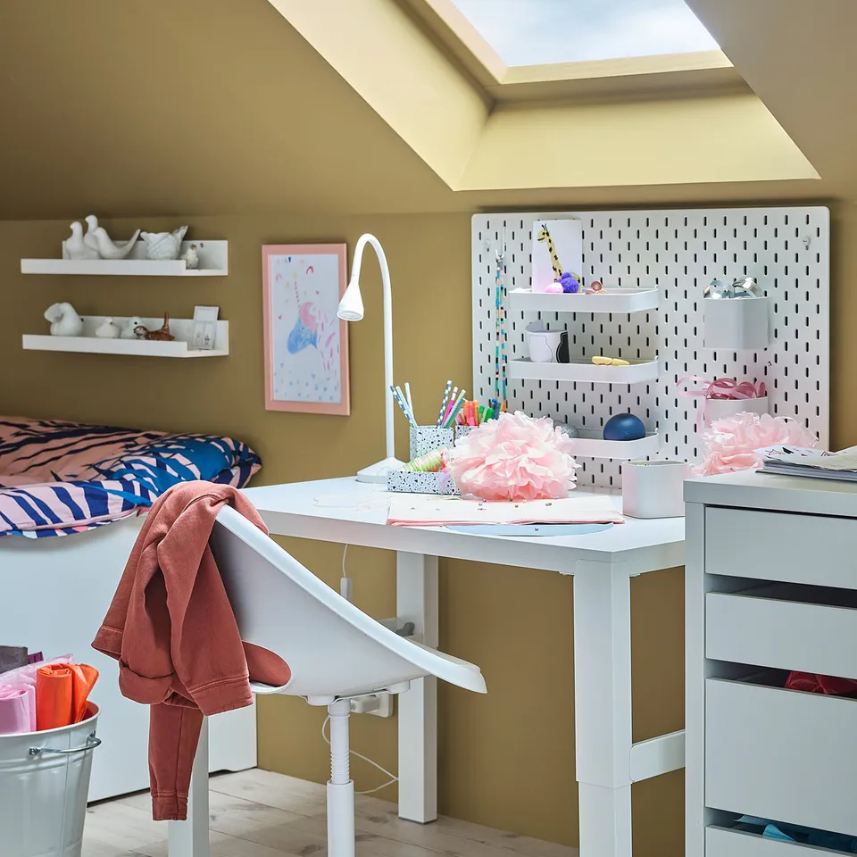 A kids room with a white LOBERGET desk chair, drawing supplies, a pegboard, and a wall lamp.