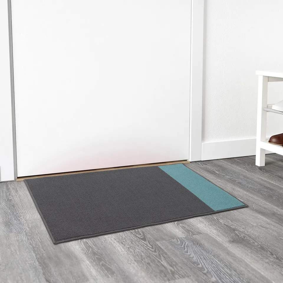 Grey door mat with a teal stripe lies near a white door. It stays in place with a backing. Easy to clean by vacuuming or shaking.