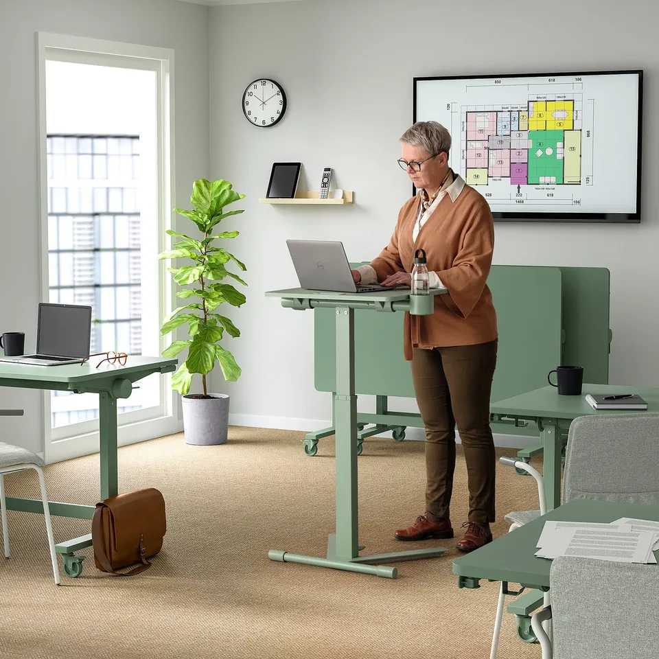 Person at height-adjustable office table with laptop, casters, plant, and mug.