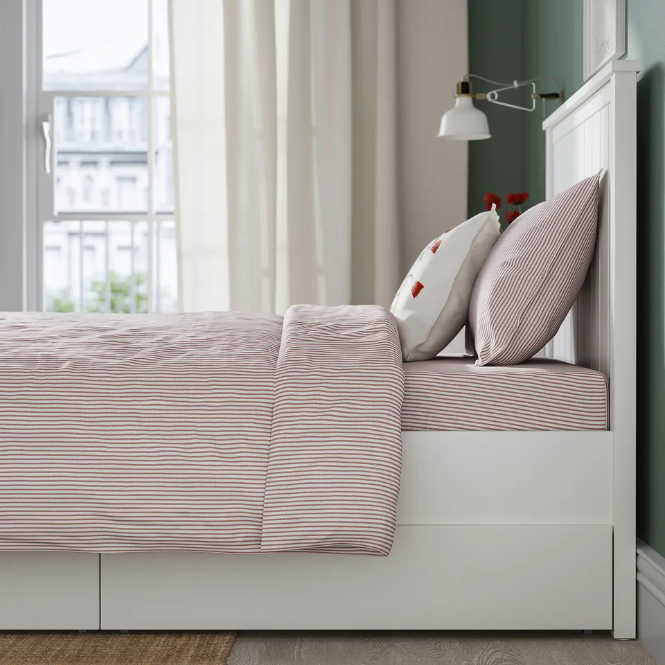 Bed with red-striped sheets, white headboard, and drawers for storage.